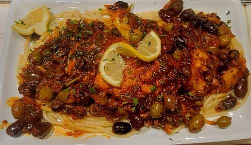 A plate of spaghetti topped with a rich tomato sauce, olives, and lemon slices, garnished with parsley.