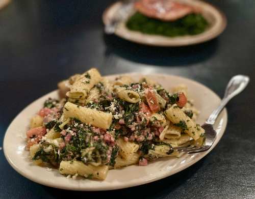 A plate of rigatoni pasta mixed with spinach, tomatoes, and feta cheese, served with a fork on the side.