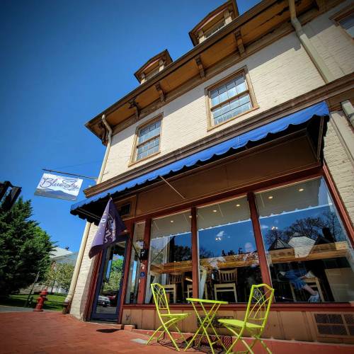 A charming café with a blue awning and bright green chairs outside, set against a clear blue sky.