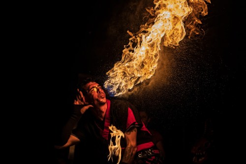 A performer breathes fire, creating a dramatic flame against a dark background, showcasing a captivating fire-eating act.