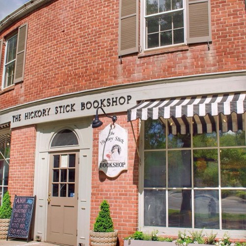 Exterior of The Hickory Stick Bookshop, featuring a brick facade, a sign, and a striped awning.