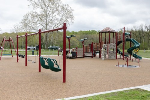 A playground featuring swings, slides, and climbing structures, set in a grassy area under a cloudy sky.