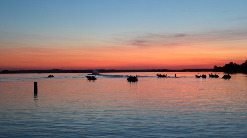 Boats on a calm lake at sunset, with vibrant orange and purple hues reflecting on the water.