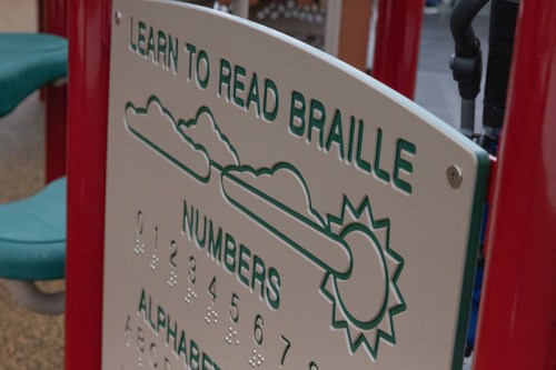 Sign featuring Braille and text for learning numbers and the alphabet, with clouds and a sun design.