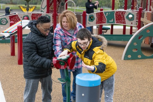 Two children and an adult interact with playground equipment in a colorful outdoor play area.
