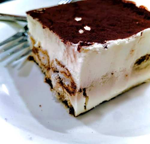 A slice of tiramisu on a plate, featuring layers of cream and cocoa powder, with two forks beside it.