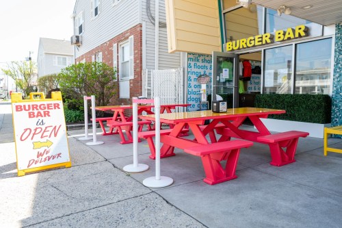 Outdoor seating area of a Burger Bar with bright red picnic tables and an open sign.