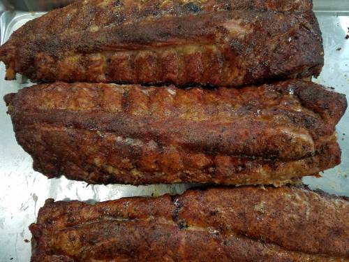 Three pieces of perfectly cooked, seasoned ribs on a silver tray, showcasing a crispy exterior and juicy texture.