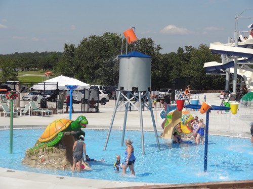 A water park scene with children playing in a pool featuring turtle sculptures and colorful water features.