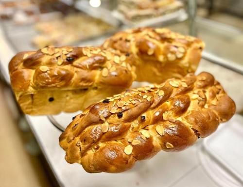 Three golden-brown braided loaves of bread topped with sliced almonds, displayed in a bakery setting.