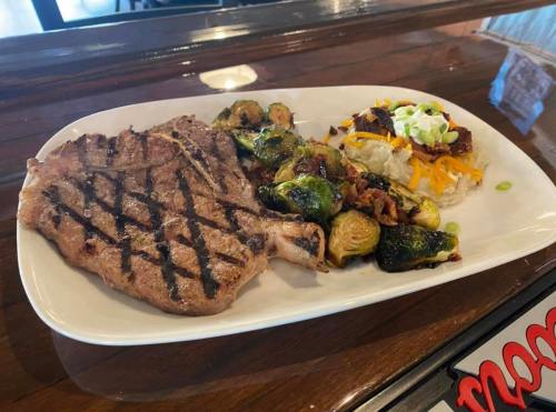 A grilled steak with Brussels sprouts and a loaded baked potato on a white plate.