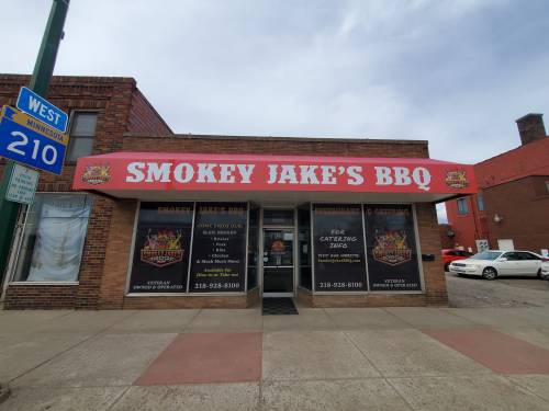 Exterior of Smokey Jake's BBQ restaurant, featuring a red awning and large signage, with a street sign nearby.