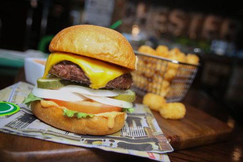 A juicy cheeseburger with lettuce, tomato, pickles, and onions, served with a side of tater tots.