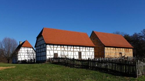 Three traditional houses with red roofs and wooden frames, set against a clear blue sky and green grass.