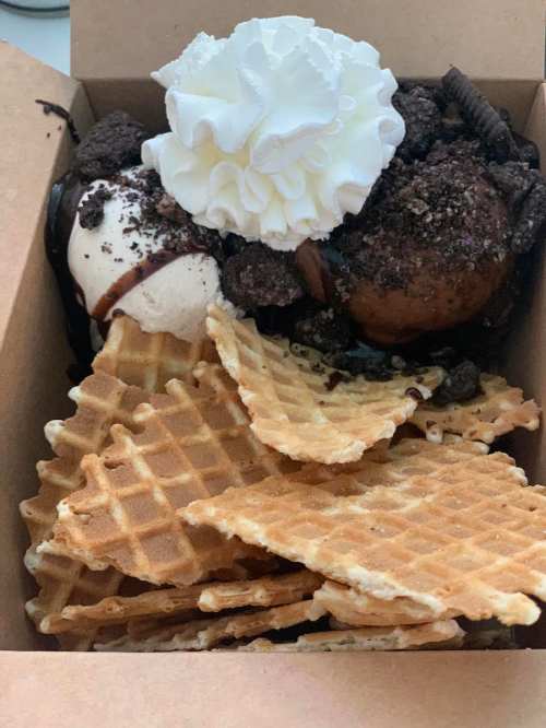 A dessert box with ice cream, crushed cookies, chocolate sauce, whipped cream, and waffle cones.