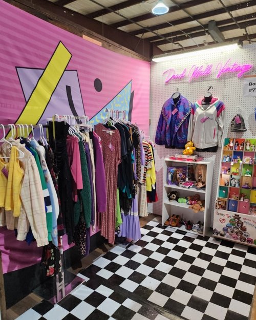 A vintage clothing display featuring colorful garments on hangers, with a pink backdrop and checkered floor.