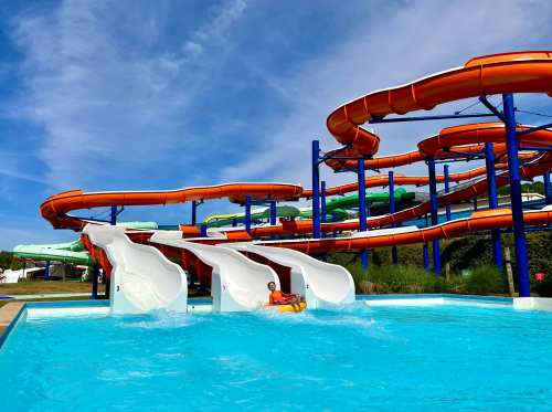 A water park featuring colorful slides and a pool, with a person sliding down one of the white slides.