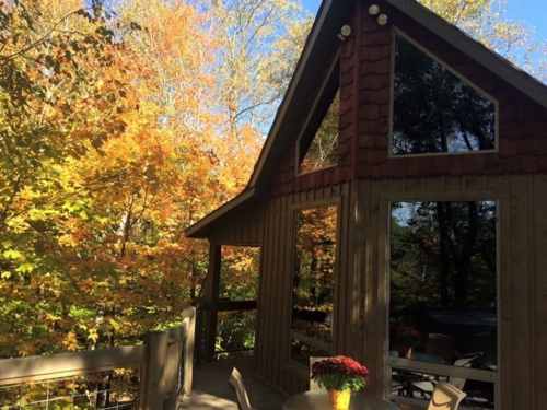 A cozy wooden cabin surrounded by vibrant autumn foliage and a clear blue sky.