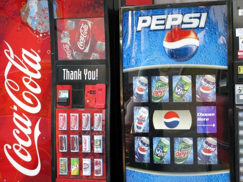 A vending machine displaying Coca-Cola and Pepsi products, with a "Thank You!" sign on the Coca-Cola side.