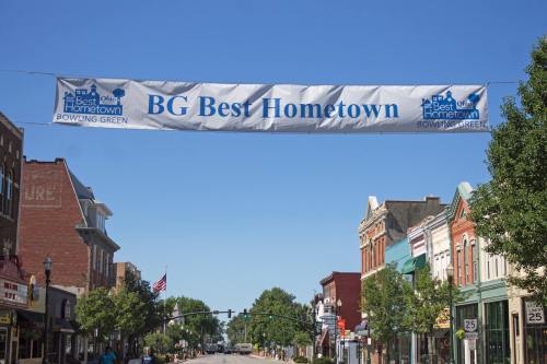 A banner reading "BG Best Hometown" hangs over a street lined with historic buildings and trees in Bowling Green.
