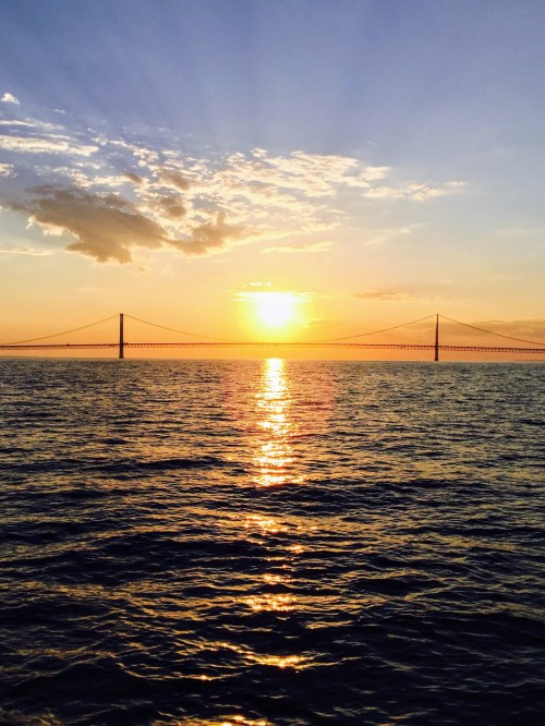 A sunset over a calm sea, with a bridge silhouetted against the colorful sky and reflecting on the water.
