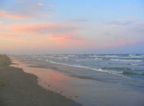 A serene beach at sunset, with gentle waves lapping at the shore and a pastel sky reflecting on the water.