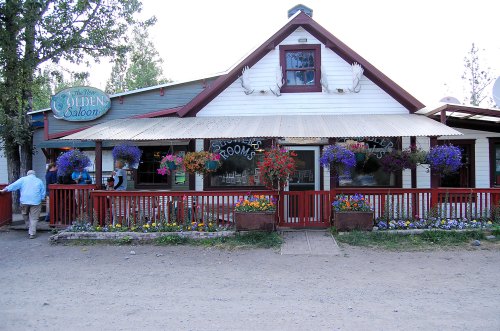 A charming saloon with colorful flower baskets, a wooden porch, and a welcoming entrance in a rustic setting.