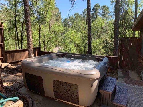 A hot tub on a wooden deck surrounded by tall trees and greenery, with bubbling water visible inside.