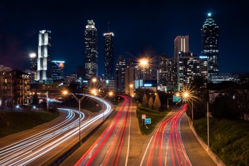 Night view of Atlanta's skyline with light trails from cars on a highway in the foreground.