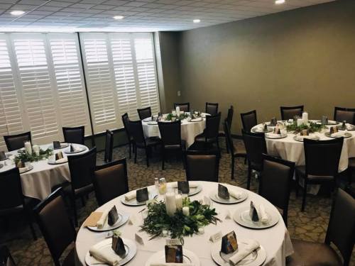 A banquet room set with round tables, white tablecloths, and greenery centerpieces, ready for an event.
