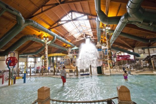 Indoor water park featuring slides, a splash area, and a large water feature under a wooden ceiling.