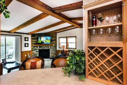 Cozy living room with wooden beams, stone fireplace, and a view of the outdoors, featuring a wine rack and glassware.