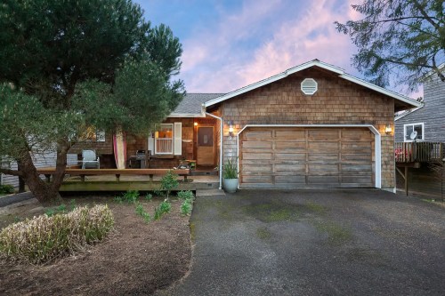 A cozy house with a wooden exterior, garage, and landscaped front yard, set against a colorful sunset sky.