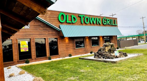 Exterior of Old Town Grill featuring wooden siding, green awning, and a small rock fountain in the foreground.