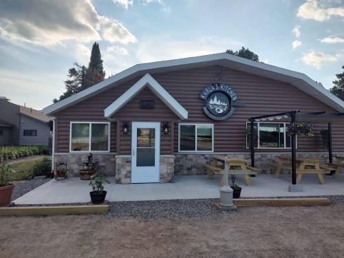Exterior of a rustic restaurant named "Karla's Kitchen," featuring a stone and wood facade, picnic tables, and a "Closed" sign.