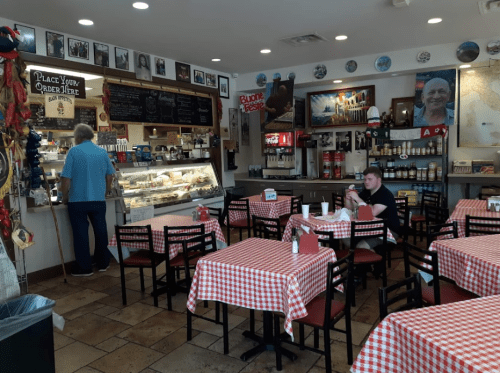 A cozy restaurant with checkered tablecloths, a counter display, and a few patrons enjoying their meals.