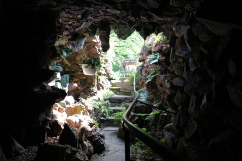 A stone passageway leads to a bright, lush garden with steps and greenery.