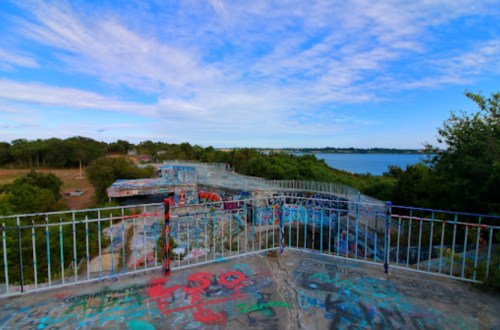 View from a graffiti-covered lookout point overlooking a lake, surrounded by trees and a blue sky.
