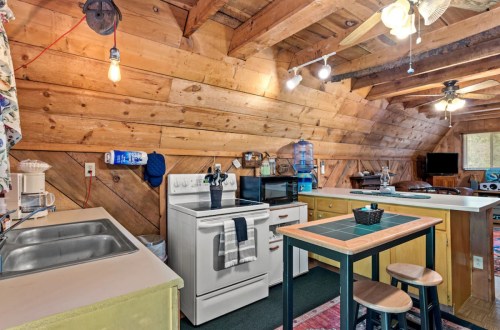 Cozy kitchen with wooden walls, a stove, sink, and a small island, featuring warm lighting and rustic decor.