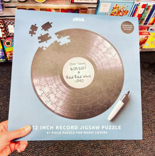 A hand holds a 12-inch record jigsaw puzzle box featuring a vinyl design and a handwritten label.