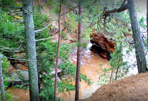A serene view of a river flowing between rocky cliffs, surrounded by lush green trees.