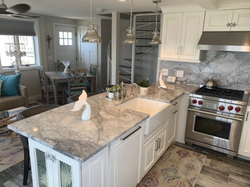 Modern kitchen with marble countertops, stainless steel appliances, and a dining area in the background. Bright and inviting space.