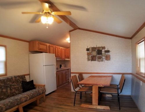Cozy interior of a small kitchen and dining area with a wooden table, chairs, and a sofa. Bright and inviting atmosphere.