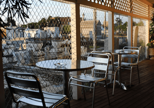A cozy outdoor café with metal tables and chairs, overlooking a scenic view through a chain-link fence.