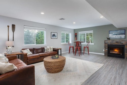 Cozy living room with a leather sofa, round coffee table, dining area, and a fireplace, surrounded by large windows.