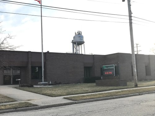 A brick building with a digital clock display, a water tower in the background, and an American flag flying.