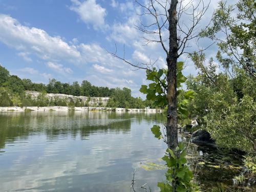 A serene lake surrounded by greenery and a rocky shoreline under a partly cloudy sky.
