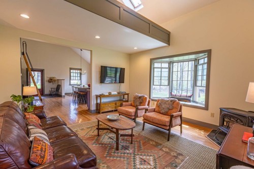 Cozy living room with a leather sofa, two armchairs, a coffee table, and large windows overlooking a garden.