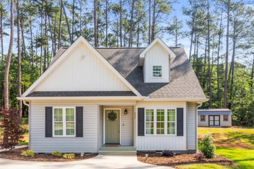 A charming two-story house with a gabled roof, surrounded by trees and a small shed in the background.
