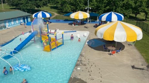 A vibrant pool area with a water slide, colorful umbrellas, and people enjoying the water on a sunny day.
